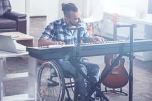 Enjoying my alternative therapy. Talented skillful positive disabled sitting in the wheelchair in the studio and enjoying music while playing the musical keyboard